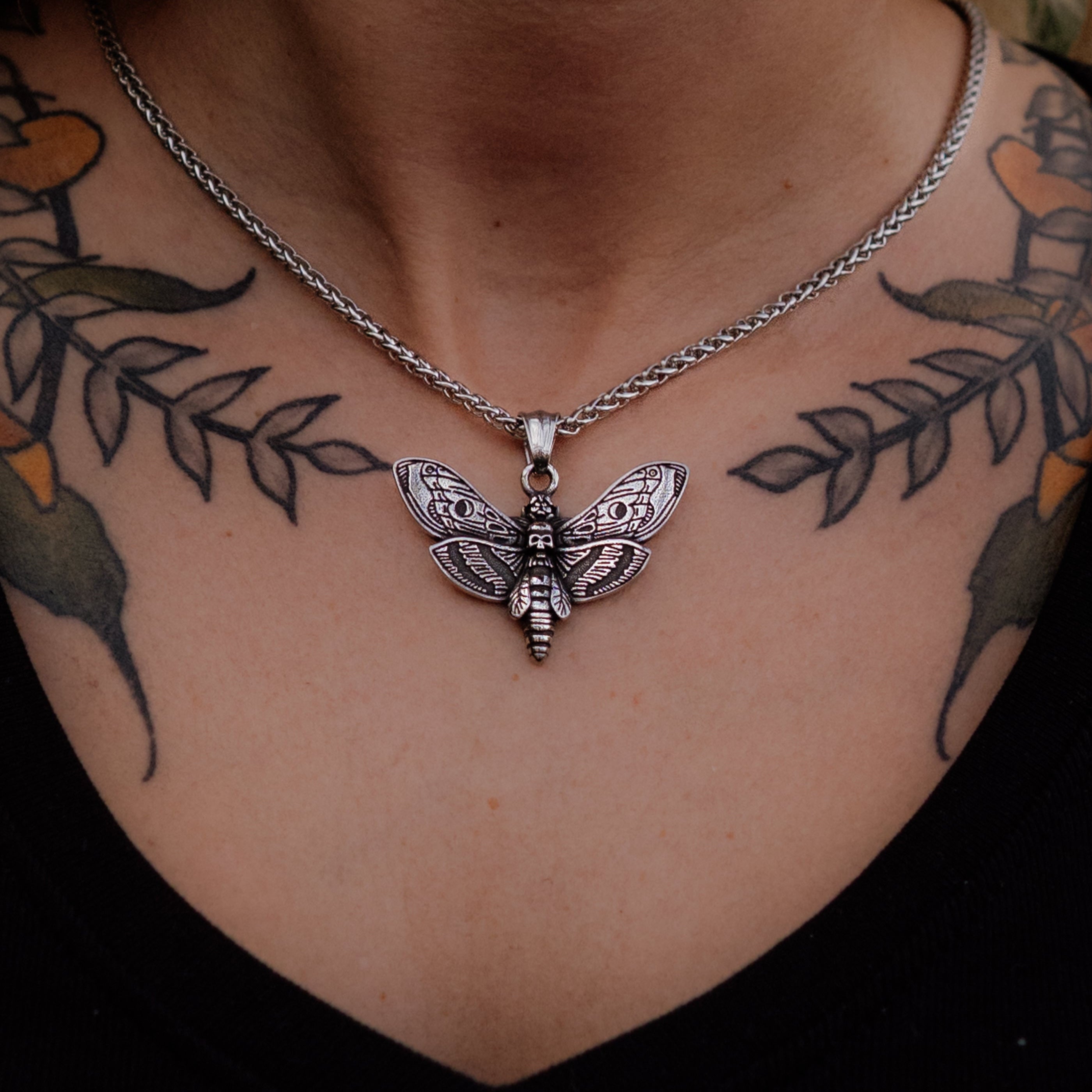 Silver butterfly pendant necklace on a person with tattoos