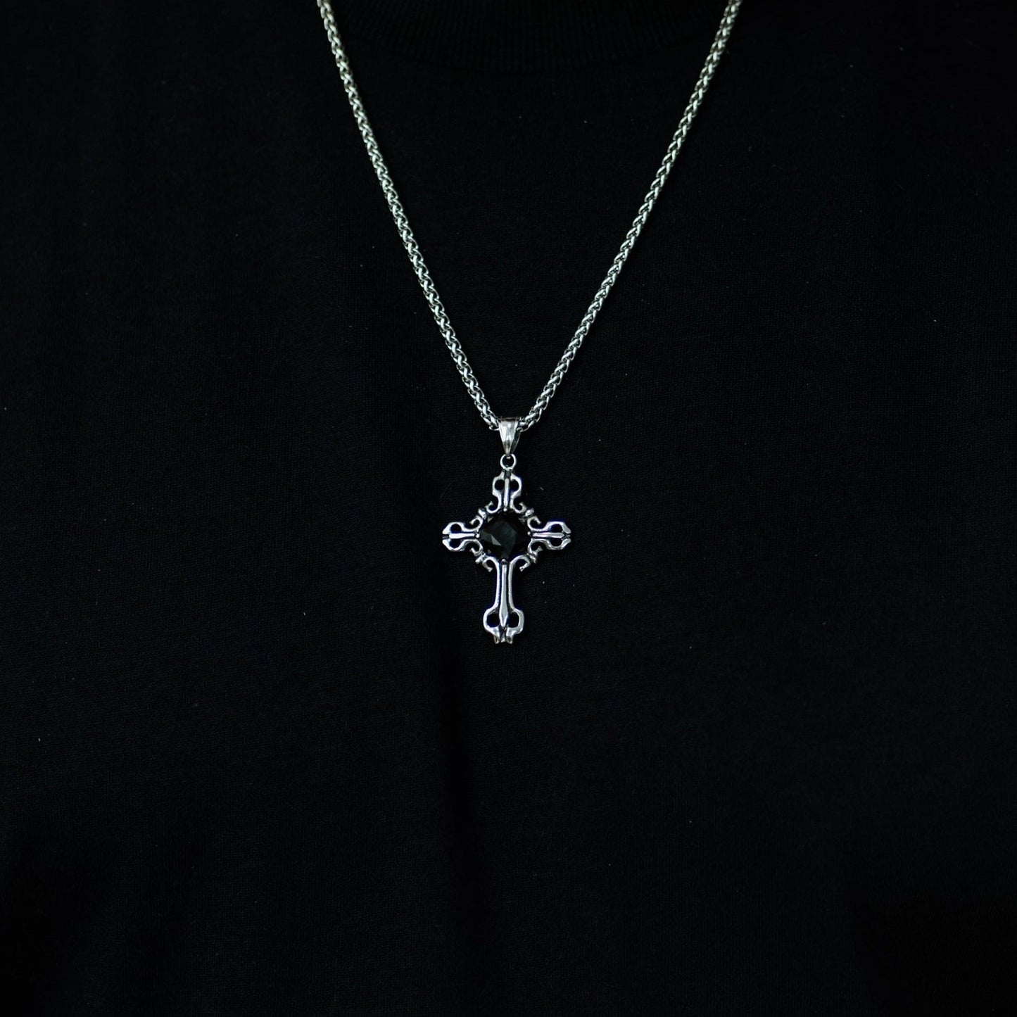 Person wearing a black shirt with a silver necklace featuring a cross pendant.