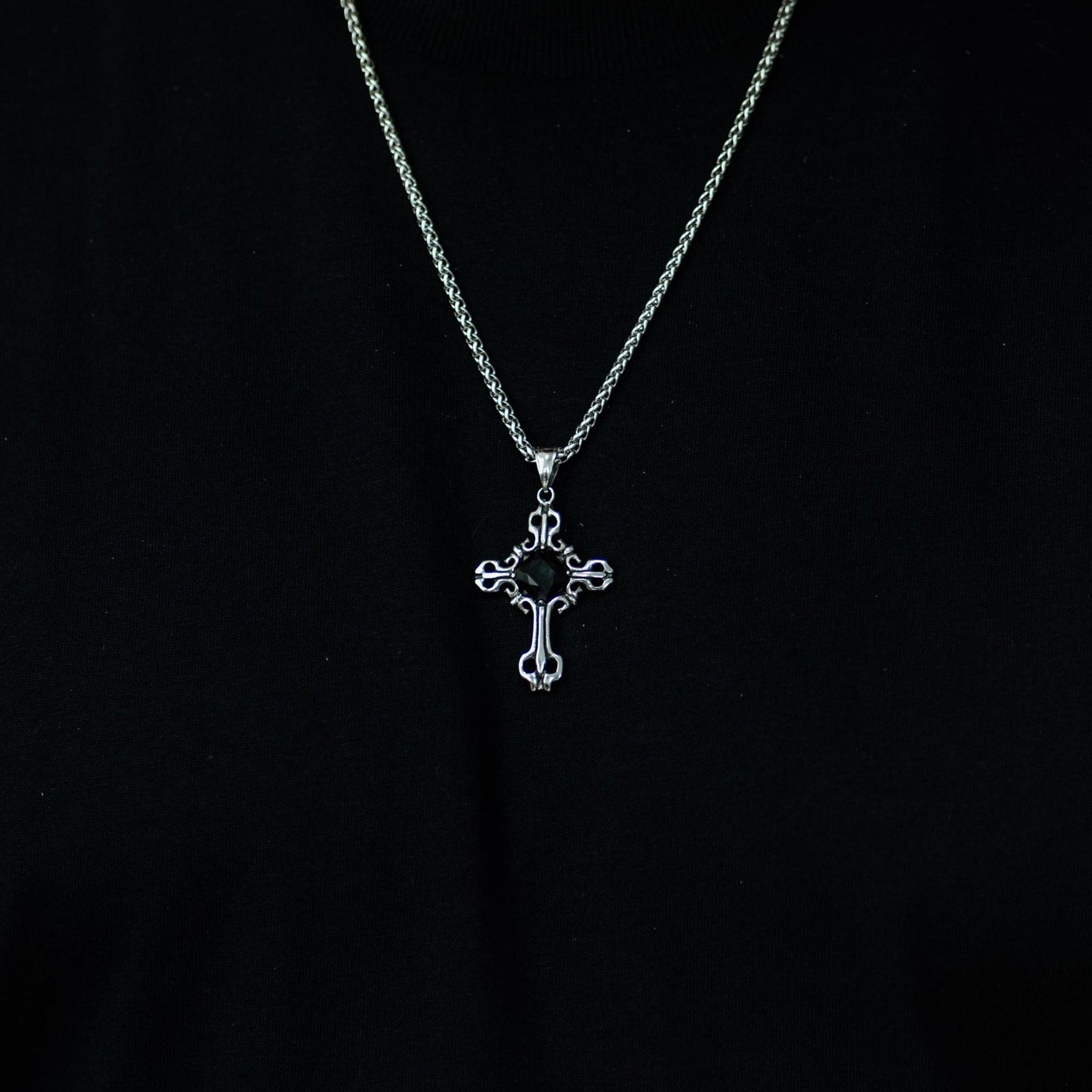 Person wearing a black shirt with a silver necklace featuring a cross pendant.