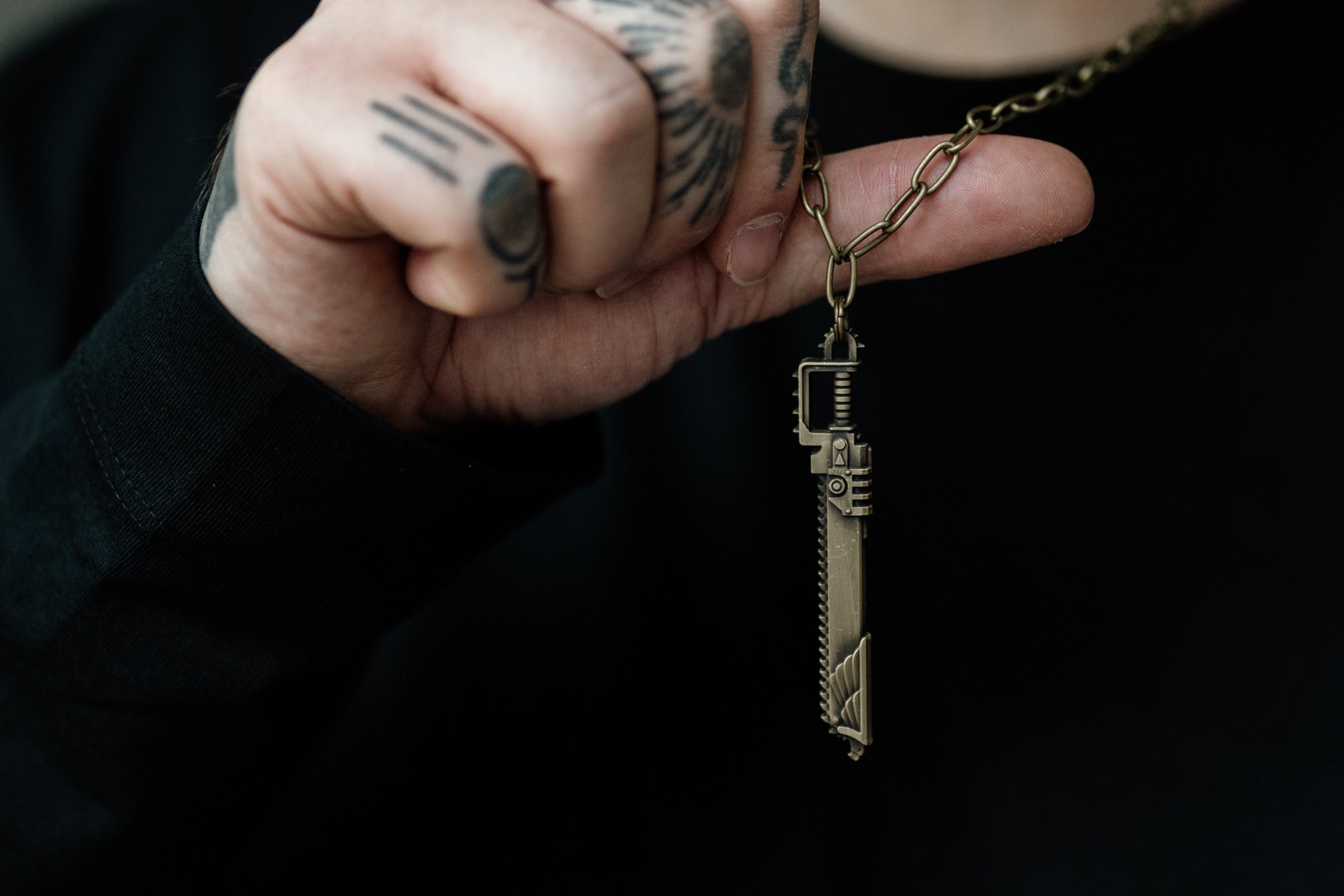 Person holding a key-shaped pendant with tattoos on fingers