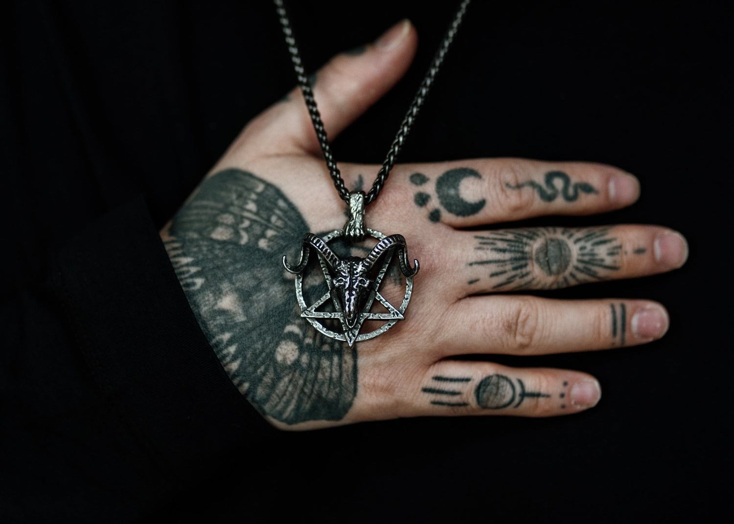 Person wearing a necklace with a pentagram pendant, hand close-up on a dark background