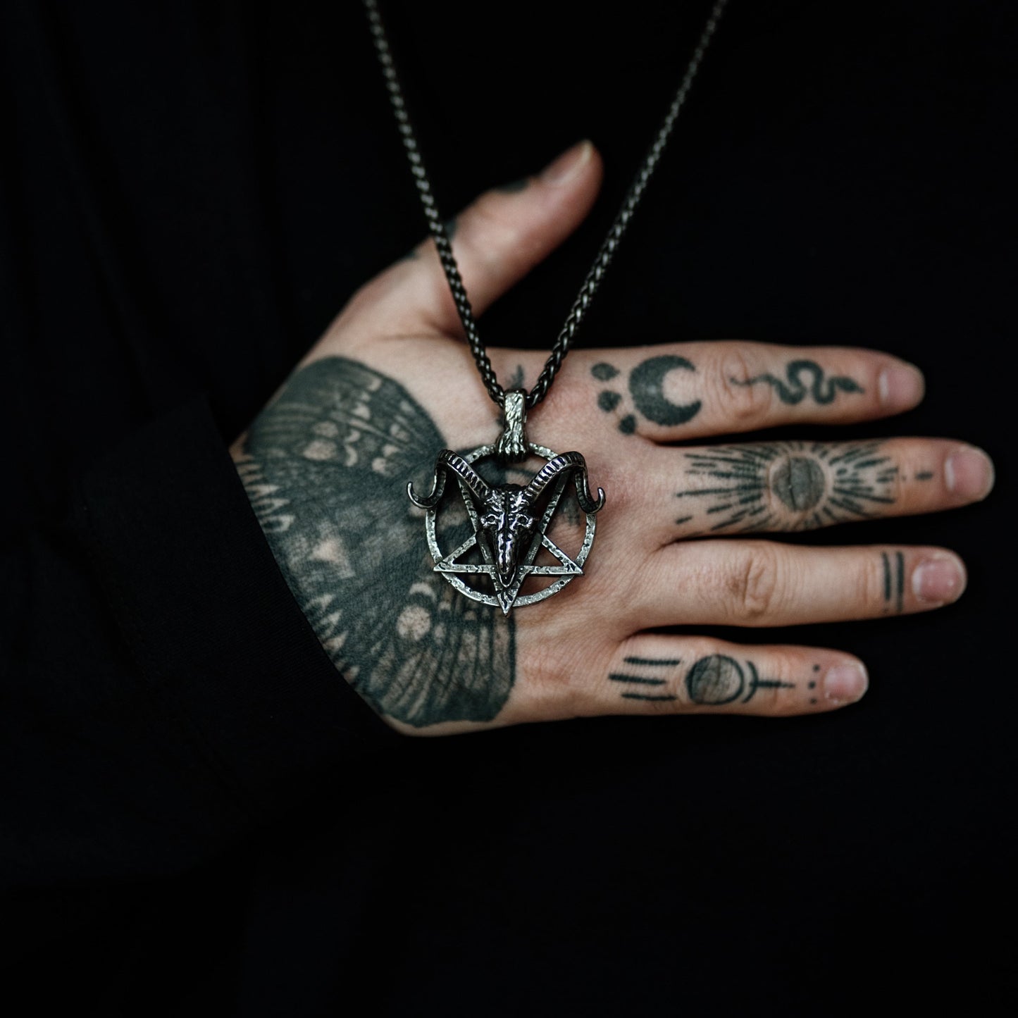 Person wearing a necklace with a pentagram pendant, hand close-up on a dark background
