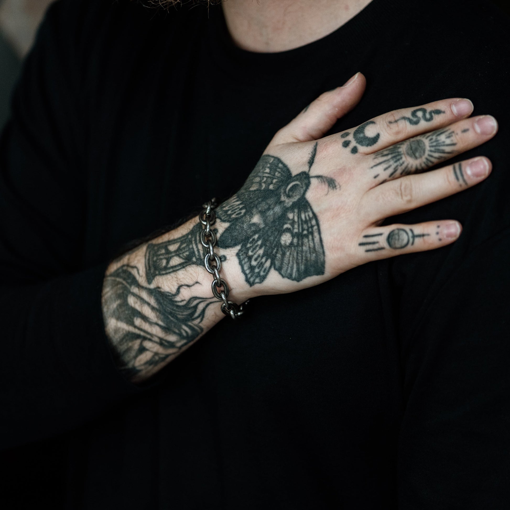 Person wearing a black shirt with tattoos on their arms and hand.