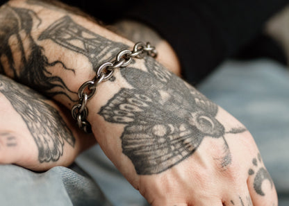 Close-up of a hand with butterfly tattoo and chain bracelet on a blurred background