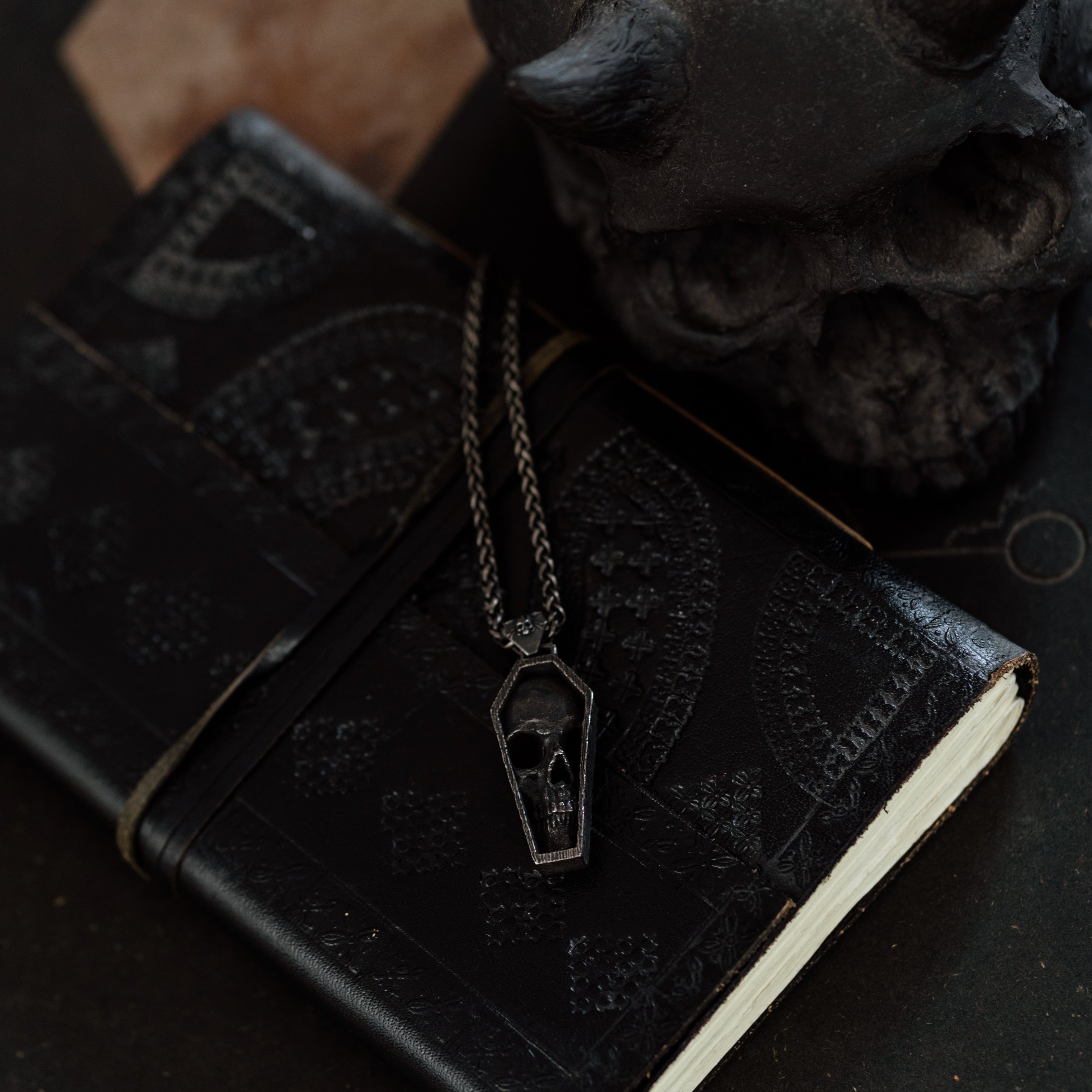 Black leather notebook with a necklace featuring a pendant on a dark surface