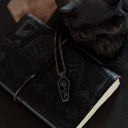 Black leather notebook with a necklace featuring a pendant on a dark surface
