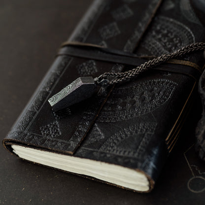 Black leather-bound notebook with chain and clasp on a dark surface