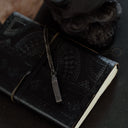 Black leather notebook with decorative stitching on a dark surface