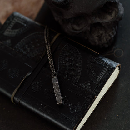Black leather notebook with decorative stitching on a dark surface