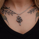 Necklace with a snake pendant worn by a person with tattoos on their neck and shoulders.
