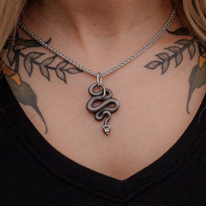 Necklace with a snake pendant worn by a person with tattoos on their neck and shoulders.