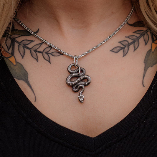 Necklace with a snake pendant worn by a person with tattoos on their neck and shoulders.