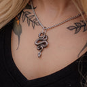 Necklace with a snake pendant worn by a person with tattoos on their neck and shoulders.