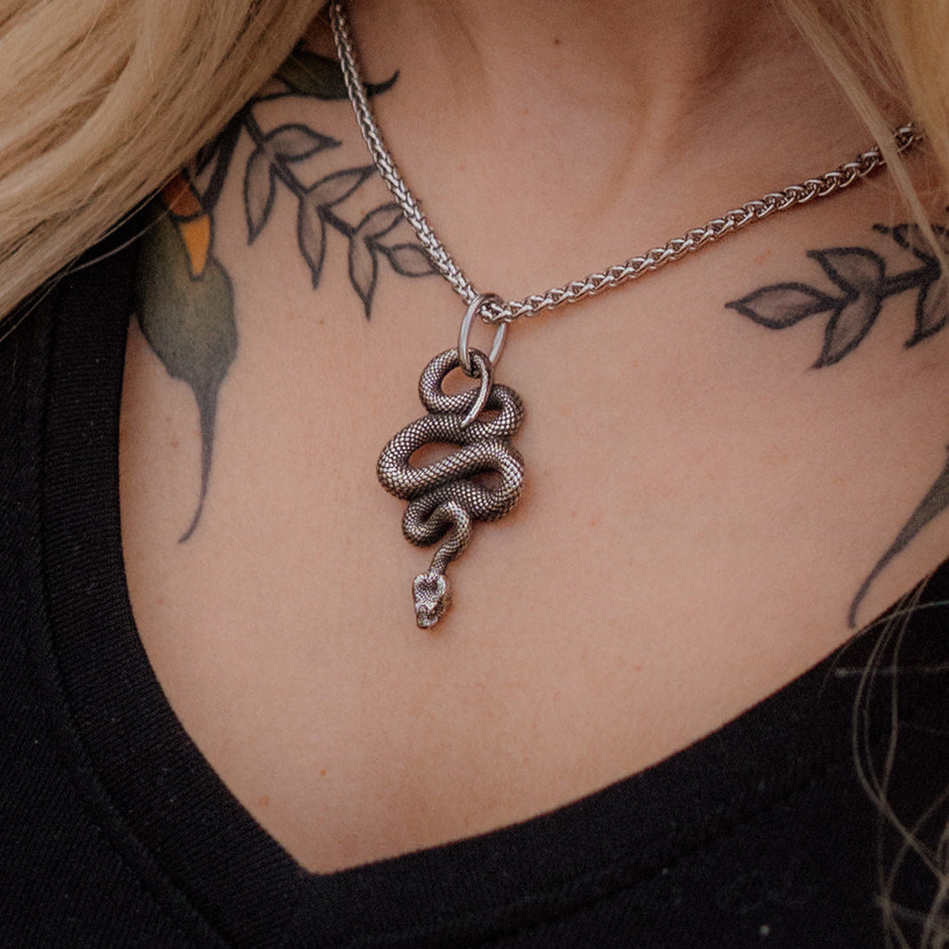 Necklace with a snake pendant worn by a person with tattoos on their neck and shoulders.