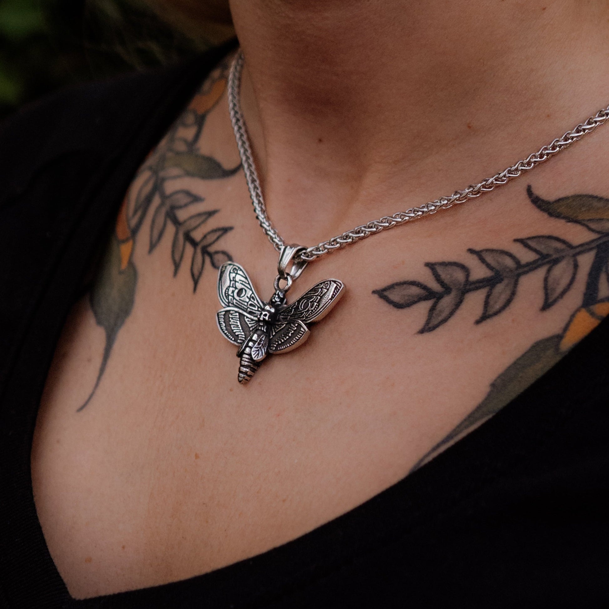 Silver butterfly necklace on a person with tattoos